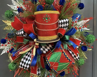 May include: A decorative wreath featuring a central red glittery top hat and a red and green drum. The arrangement includes black and white chequered ribbons, blue velvet spheres, red berries, gold foliage, and green glittery ornaments.