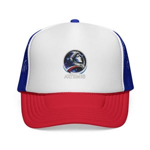 May include: A red, white, and blue trucker hat with a circular graphic of an astronaut in a helmet against a starry background. The word "ARTEMIS" is printed below the graphic. The hat has a white front panel, a red peak, and a blue mesh back.