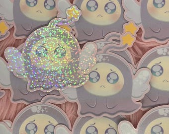 May include: A collection of stickers featuring a cute, cartoonish ghost character with large, expressive eyes and small angel wings. One sticker has a holographic, glittery finish, while the others have a matte appearance. The ghost is wearing a hooded outfit.