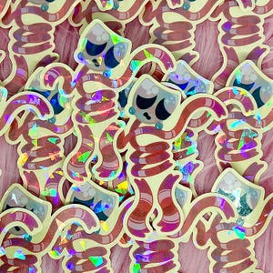 May include: A collection of stickers featuring a cartoonish figure with a cream-colored body, red and pink striped arms and legs, and a face with black eyes and a sad expression. The stickers have a holographic, iridescent effect.