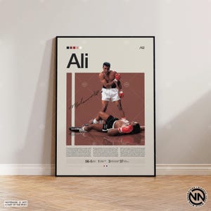 Puede incluir: Un póster enmarcado con una escena de boxeo con el nombre "Ali". La imagen muestra a un boxeador de pie sobre un oponente derrotado. El póster incluye estadísticas y una firma.