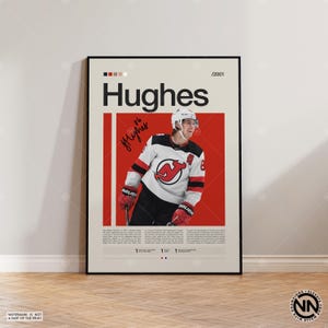 May include: A framed poster with the name "Hughes" in black lettering, above a photo of a hockey player in a white, black, and red jersey. The poster includes the player's signature and the number 8. The background is cream with a red rectangle.