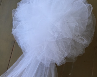 May include: A large, round, white tulle decoration with a layered, cloud-like appearance. A long, flowing tulle tail extends from the base. The tulle is soft and delicate, suitable for weddings or other special events.