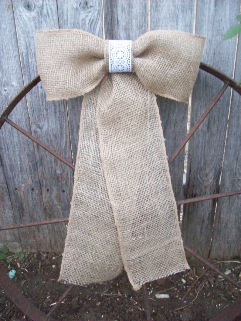 May include: A large burlap bow with a white lace center, tied to a rusty metal fence.