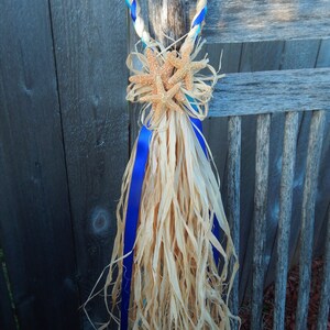 May include: A blue and turquoise braided rope with a starfish decoration and a long, flowing, natural fiber tassel. The rope is tied around a wooden post.