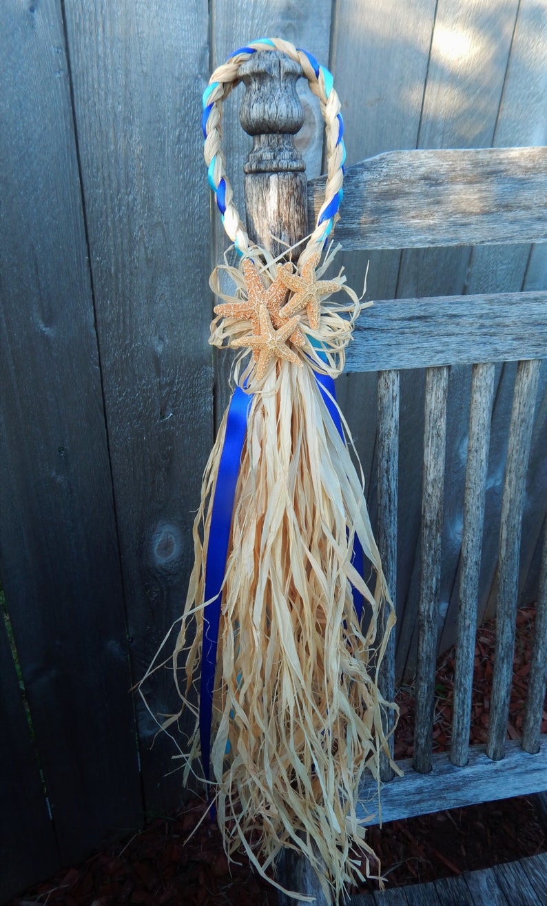 May include: A blue and turquoise braided rope with a starfish decoration and a long, flowing, natural fiber tassel. The rope is tied around a wooden post.