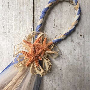 May include: A blue and white braided rope with a starfish decoration. The rope is tied into a loop and the starfish is attached to the rope with a brown ribbon.