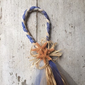 May include: A white and blue rope wreath with a brown starfish and straw bow decoration.