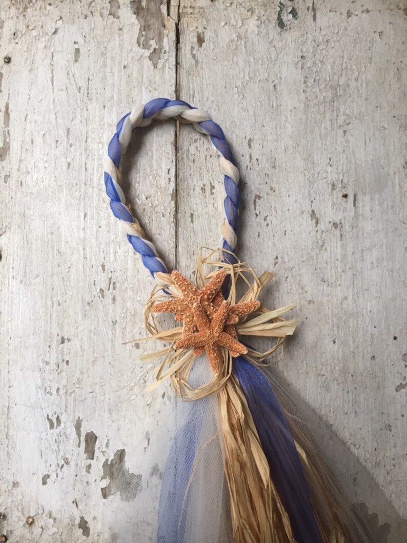 May include: A white and blue rope wreath with a brown starfish and straw bow decoration.