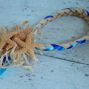 May include: A braided straw wreath with blue and turquoise ribbon accents, decorated with three starfish.