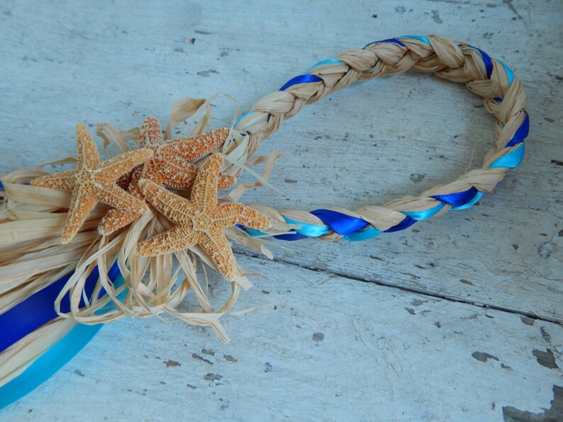 May include: A braided straw wreath with blue and turquoise ribbon accents, decorated with three starfish.