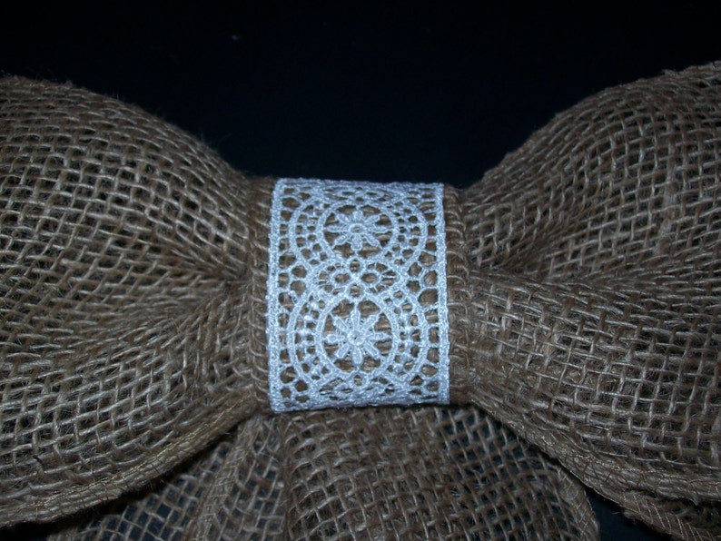 May include: A brown burlap bow with a white lace trim. The bow is tied in the center with a white lace ribbon.