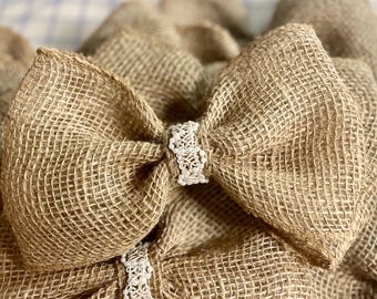 May include: A close-up of a burlap bow with a white, beaded embellishment. The bow is made of natural burlap fabric and has a rustic, handmade look.