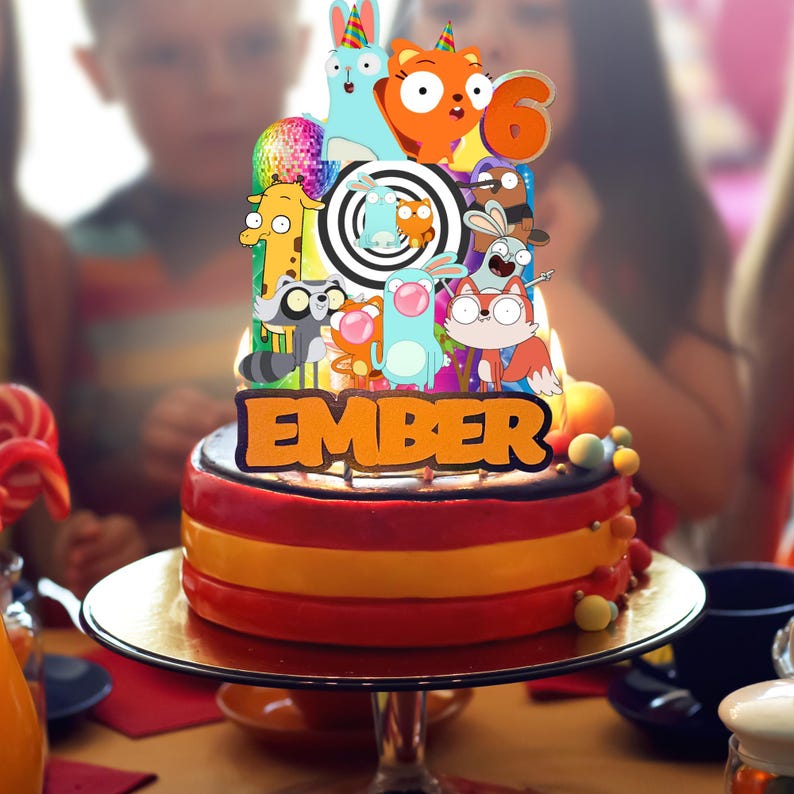 Op de afbeelding: Een verjaardagstaarttopper met meerdere lagen, voorzien van een kleurrijke reeks cartoon-dierfiguren, een discobal en een zwart-wit spiraalpatroon. De naam EMBER staat in grote oranje letters aan de basis, met het cijfer 6 erbovenop.