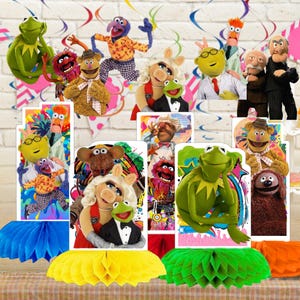 May include: A collection of Muppet Show character cutouts and figurines, including Kermit the Frog, Miss Piggy, Fozzie Bear, and Gonzo. The scene is decorated with colorful honeycomb centerpieces and hanging streamers, creating a festive atmosphere.