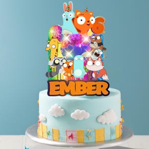 Op de afbeelding: Een lichtblauwe taart versierd met witte wolken en een gele banner, bekroond met een kleurrijke taarttopper met stripfiguren, een discobal, het cijfer 6 en de naam EMBER in grote oranje letters met een donkere omlijning.