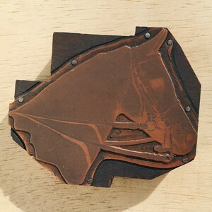 May include: A close-up of a wooden printing block with a copper plate depicting a horse's head. The horse's head is in profile, with its mane and bridle visible. The block is secured with metal tacks.