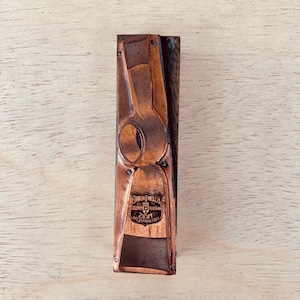 May include: A vintage copper and wood printing block with an axe design. The copper has a dark patina and is riveted to a rectangular wooden base. The block includes the text "KLEIN TOOLS" and other text.
