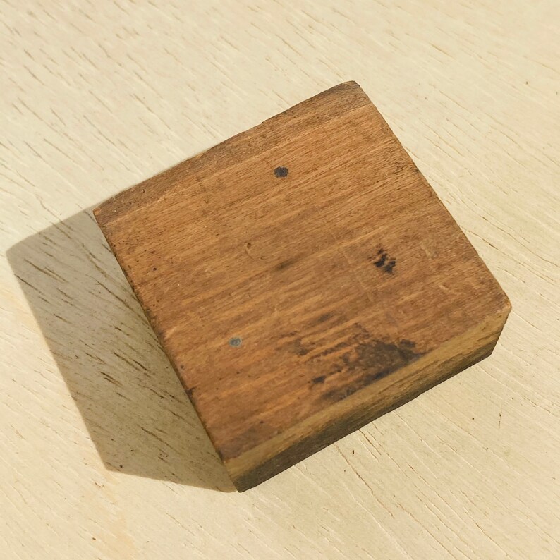 Pu&ograve; includere: Un piccolo blocco di legno quadrato con una finitura marrone naturale. Il legno ha una texture leggermente ruvida e mostra segni di usura.