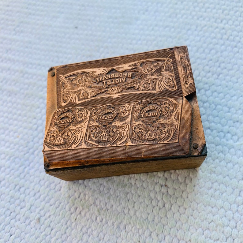 Puede incluir: Un bloque de impresi&oacute;n de madera con un dise&ntilde;o intrincado que presenta las palabras "VIOLET REDBREAST". El bloque tiene cuatro cuadrados m&aacute;s peque&ntilde;os con la palabra "VIOLET" en relieve en cada uno.