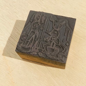 Pu&ograve; includere: Un blocco di stampa in legno vintage con un'immagine intagliata di una persona e un coniglio. Il blocco &egrave; di colore marrone scuro e ha una superficie usurata.