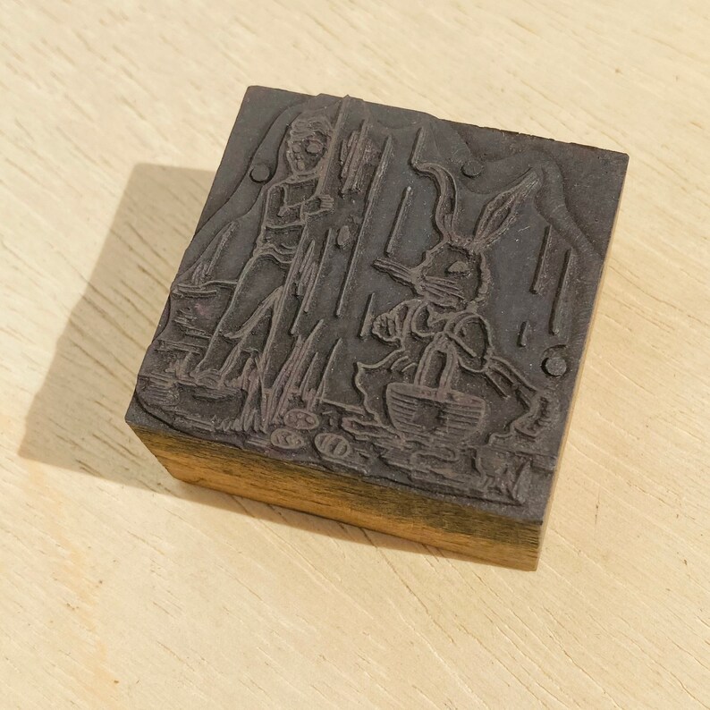 Pu&ograve; includere: Un blocco di stampa in legno vintage con un'immagine intagliata di una persona e un coniglio. Il blocco &egrave; di colore marrone scuro e ha una superficie usurata.