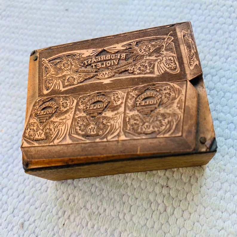 Puede incluir: Un bloque de impresi&oacute;n de madera vintage con las palabras "VIOLET REDBREAST" y "VIOLET" en relieve. El bloque tiene un dise&ntilde;o decorativo con motivos florales.