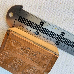 Puede incluir: Una caja de madera vintage con una tapa de metal de color lat&oacute;n. La caja tiene un dise&ntilde;o en relieve con las palabras "Red Velvet" y "Violet" en la parte superior. La caja se est&aacute; midiendo con una regla que dice "& 12 PT. AGATE INCHES".