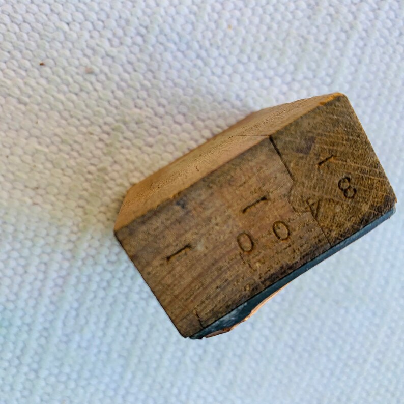 Puede incluir: Un bloque de madera con los n&uacute;meros "1000" y "18" estampados en &eacute;l. El bloque es marr&oacute;n y tiene un borde negro.