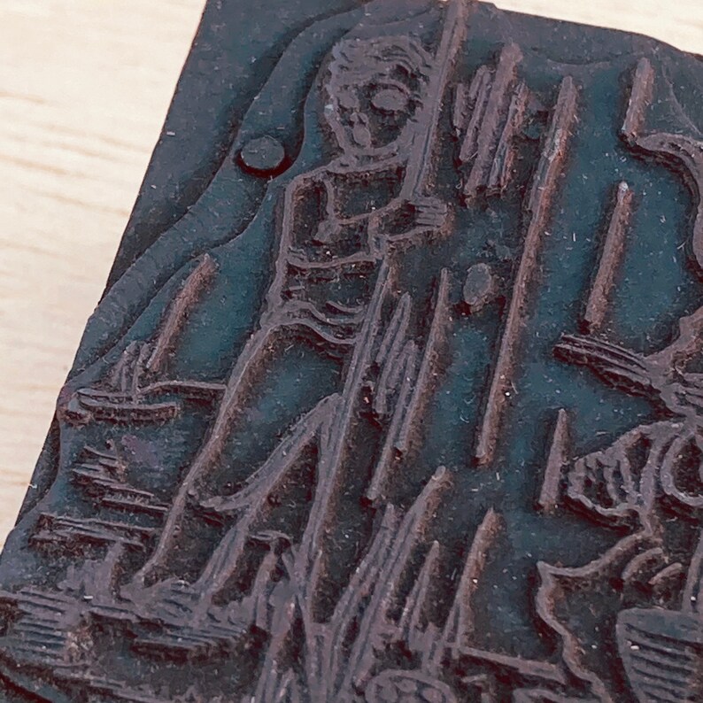Pu&ograve; includere: Un timbro da stampa in legno vintage con un design dettagliato di una persona in piedi accanto a una struttura alta. Il blocco di legno &egrave; di colore marrone scuro e ha una superficie usurata e testurizzata.