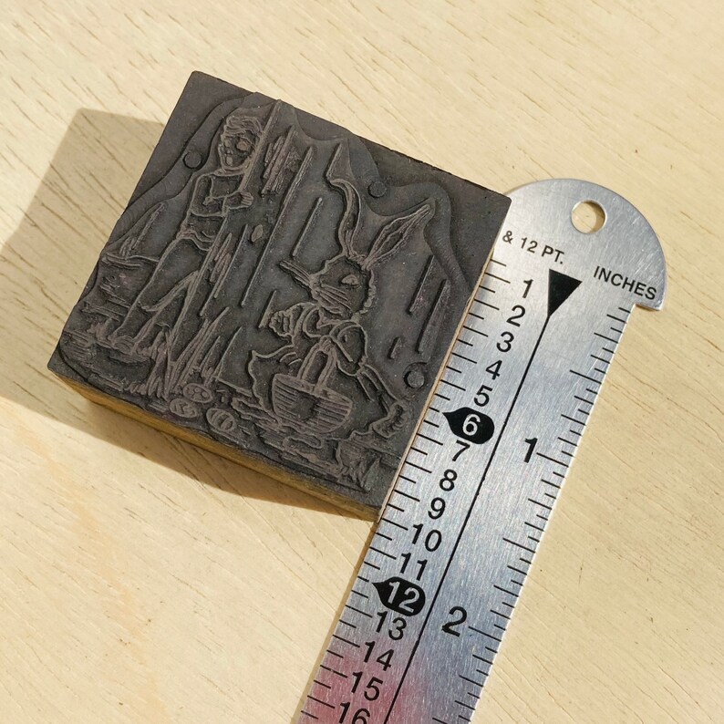 Pu&ograve; includere: Un timbro da stampa in legno vintage con un'illustrazione in bianco e nero di un coniglio e una persona che tiene un cestino. Il timbro misura circa 5 cm di larghezza.