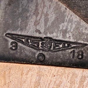 May include: Close-up of a black metal tag with a silver aeroplane logo and the text "3 0 18".