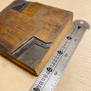May include: A close-up of a wooden printing block with a metal plate. The plate has the text "WM. RICE & CO. CEREALS" engraved on it. The block is being measured with a ruler, which shows that it is approximately 7.6 cm wide.