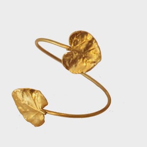 Peut inclure: Un bracelet doré en forme de feuille. Le bracelet présente deux feuilles texturées reliées par une bande incurvée. Les feuilles sont positionnées aux extrémités opposées de la bande, créant un design unique inspiré de la nature.