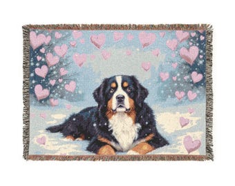 Puede incluir: Una manta tejida con un perro de montaña bernés en la nieve, rodeado de corazones rosas. El perro tiene pelo negro, marrón y blanco. El fondo es azul claro. La manta tiene un borde con flecos.