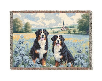 May include: Woven throw blanket featuring two Bernese Mountain Dogs in a field of blue flowers. The background depicts a rural landscape with a church and trees. The blanket has a fringed edge.