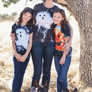 Peut inclure: Trois t-shirts &agrave; manches courtes avec des motifs tie-dye. Un t-shirt pr&eacute;sente un motif de fant&ocirc;me blanc, un autre un fant&ocirc;me blanc, et le troisi&egrave;me un visage de citrouille orange. Deux bouledogues fran&ccedil;ais portent des bandanas tie-dye assortis.