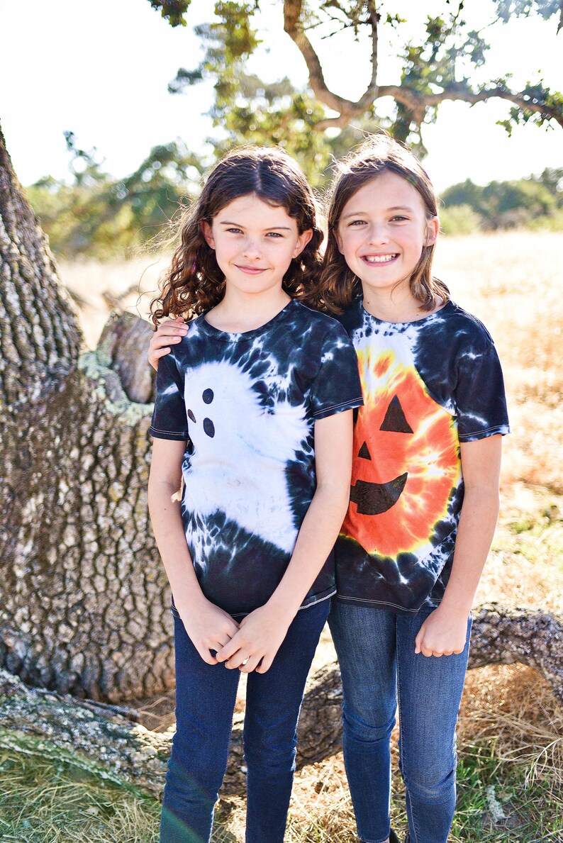 Peut inclure: Deux t-shirts &agrave; manches courtes et col rond. L'un pr&eacute;sente un motif de fant&ocirc;me blanc sur un fond tie-dye noir et blanc. L'autre affiche un motif de visage de citrouille orange sur un fond tie-dye noir, orange et blanc.