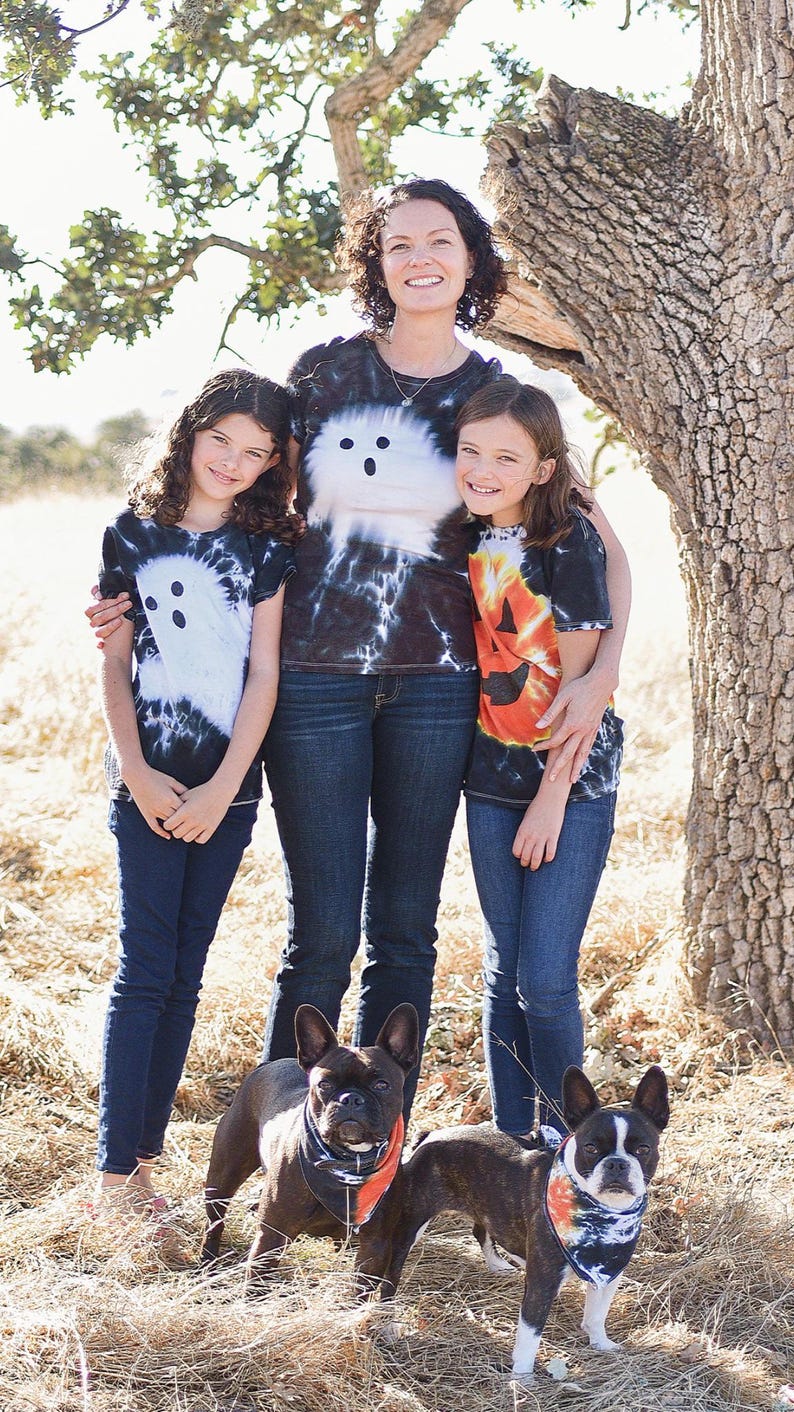 Peut inclure: Trois t-shirts &agrave; manches courtes avec des motifs tie-dye. Un t-shirt pr&eacute;sente un motif de fant&ocirc;me blanc, un autre un fant&ocirc;me blanc, et le troisi&egrave;me un visage de citrouille orange. Deux bouledogues fran&ccedil;ais portent des bandanas tie-dye assortis.
