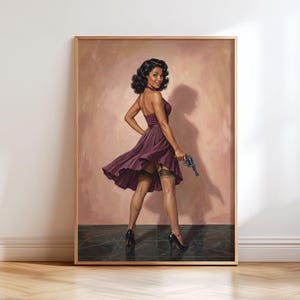 May include: Framed artwork depicting a vintage-style illustration of a woman in a purple dress holding a blue handgun. The woman wears black heels and a garter. The background is a soft pink, and the artwork is in a wooden frame.