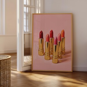 Digital art print of classic gold lipsticks in various pink and red hues, displayed in a wooden frame leaning near a softly lit window — feminine retro wall decor.