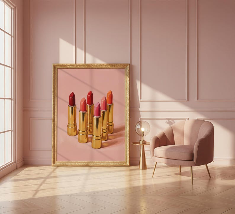 A framed retro lipstick poster featuring six golden lipsticks in shades of red, pink, and coral against a pink background, leaning on a blush wall beside a velvet armchair and gold lamp. The scene is bathed in soft sunlight, creating a luxurious, feminine, and retro-inspired atmosphere.