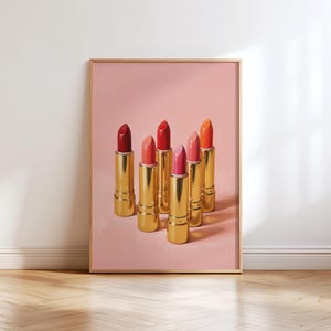 Printable wall art featuring six gold lipsticks in shades of red, coral, and pink on a soft pink background — elegant retro makeup illustration for vanity or dressing room decor.