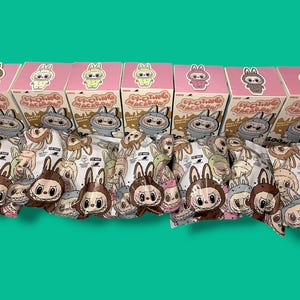 K&ouml;nnte beinhalten: Eine Sammlung von Sammler-Vinylfiguren und -Boxen. Die rosa Boxen zeigen Illustrationen von Hasenfiguren. Die Figuren befinden sich in einer transparenten Verpackung mit verschiedenen Designs zum Thema Hase. Der Text "EXCITING MACARON" ist auf den Boxen zu sehen.