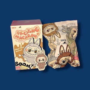K&ouml;nnte beinhalten: Eine Schachtel und eine T&uuml;te mit Sammelspielzeug mit Cartoon-Monster-Charakteren. Die Schachtel ist mit "Exciting Macaron" und "The Monsters" beschriftet, mit einem Cartoon-Hasencharakter. Die T&uuml;te ist mit verschiedenen Monstergesichtern bedruckt.