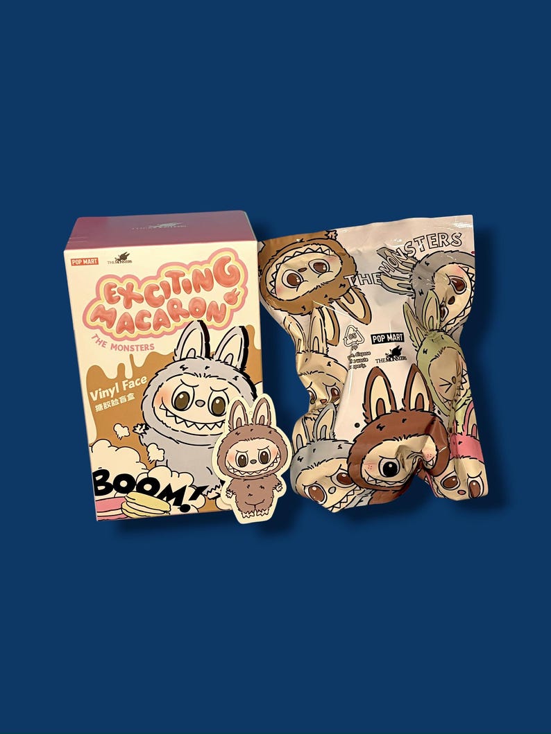 K&ouml;nnte beinhalten: Eine Schachtel und eine T&uuml;te mit Sammelspielzeug mit Cartoon-Monster-Charakteren. Die Schachtel ist mit "Exciting Macaron" und "The Monsters" beschriftet, mit einem Cartoon-Hasencharakter. Die T&uuml;te ist mit verschiedenen Monstergesichtern bedruckt.