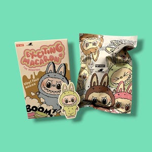 K&ouml;nnte beinhalten: Ein Sammlerspielzeug-Set mit "The Monsters"-Charakteren. Das Set enth&auml;lt eine Box mit dem Text "Exciting Macaron" und einen Blind Bag mit Charakterillustrationen. Ein kleiner Aufkleber eines Charakters ist ebenfalls vorhanden.