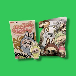 K&ouml;nnte beinhalten: Eine Pop Mart Produktdarstellung mit einer Box und einer T&uuml;te mit Cartoon-Monster-Designs. Auf der Box steht "Exciting Macaron" und "The Monsters". Ein Aufkleber eines Monsters in einem Hasenkost&uuml;m ist ebenfalls vorhanden. Die T&uuml;te ist mit verschiedenen Monsterfiguren gef&uuml;llt.