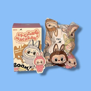 K&ouml;nnte beinhalten: Eine rosa-cremefarbene Schachtel mit dem Text "EXCITING MACARON" und "THE MONSTERS" neben einer Cartoon-Hasenfigur. Eine Blindbox und ein Aufkleber mit &auml;hnlichen Hasenfiguren sind ebenfalls vorhanden.