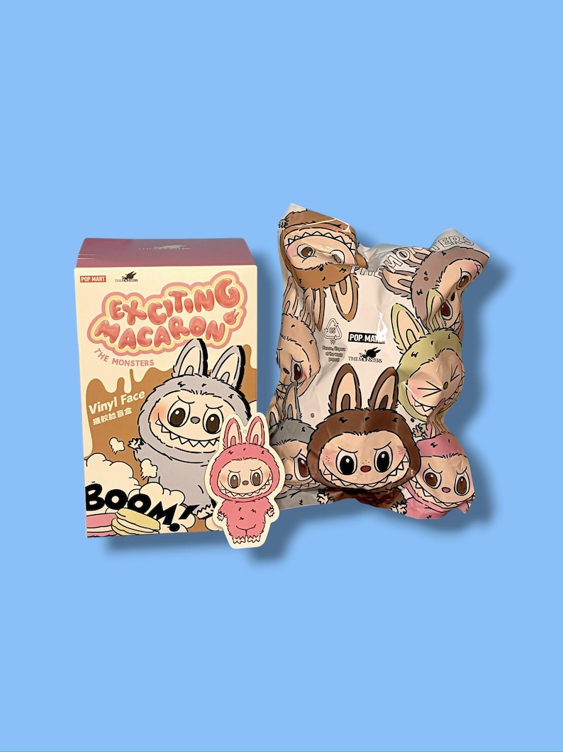 K&ouml;nnte beinhalten: Eine rosa-cremefarbene Schachtel mit dem Text "EXCITING MACARON" und "THE MONSTERS" neben einer Cartoon-Hasenfigur. Eine Blindbox und ein Aufkleber mit &auml;hnlichen Hasenfiguren sind ebenfalls vorhanden.